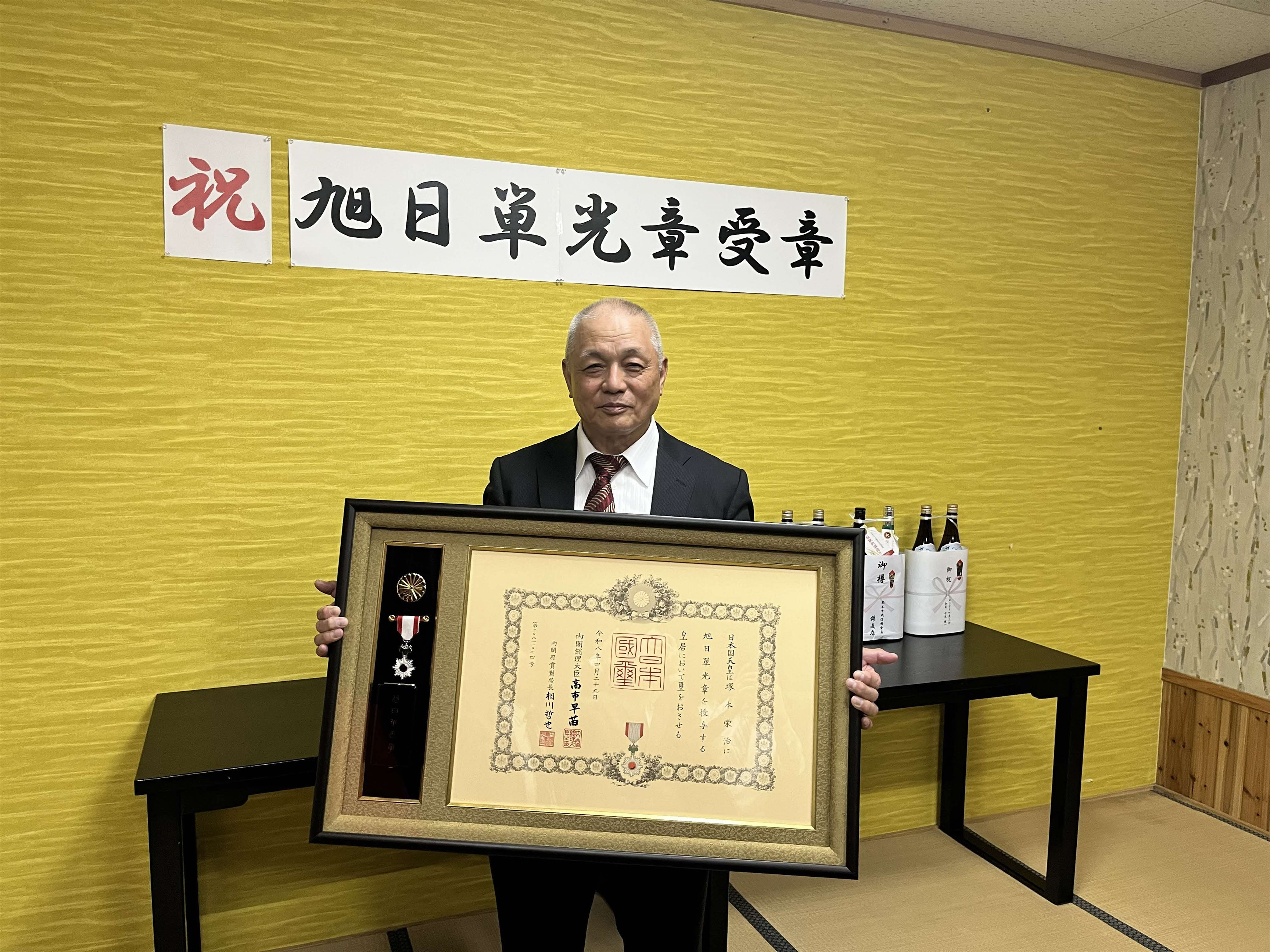 勲章と賞状を手にした塚本会長